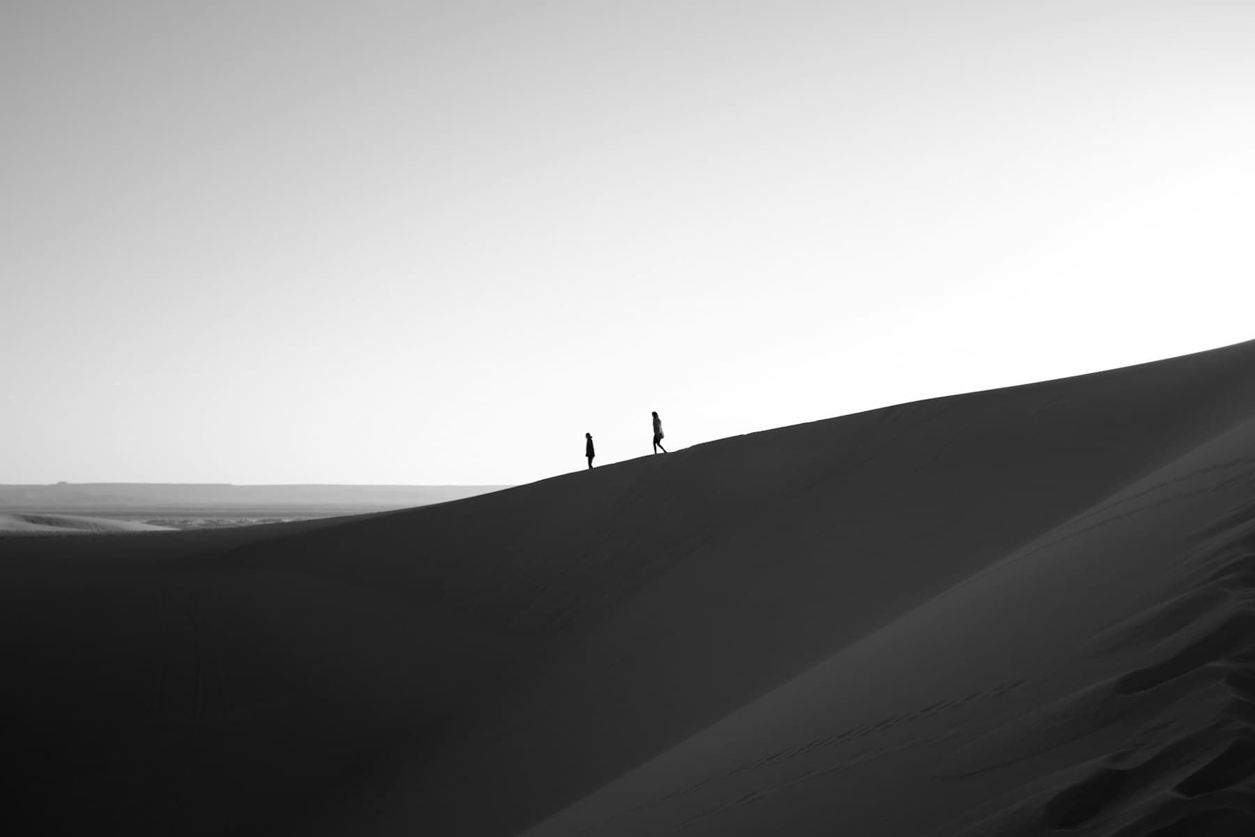 Two travellers walking along a dune ridge in the Sahara at dusk