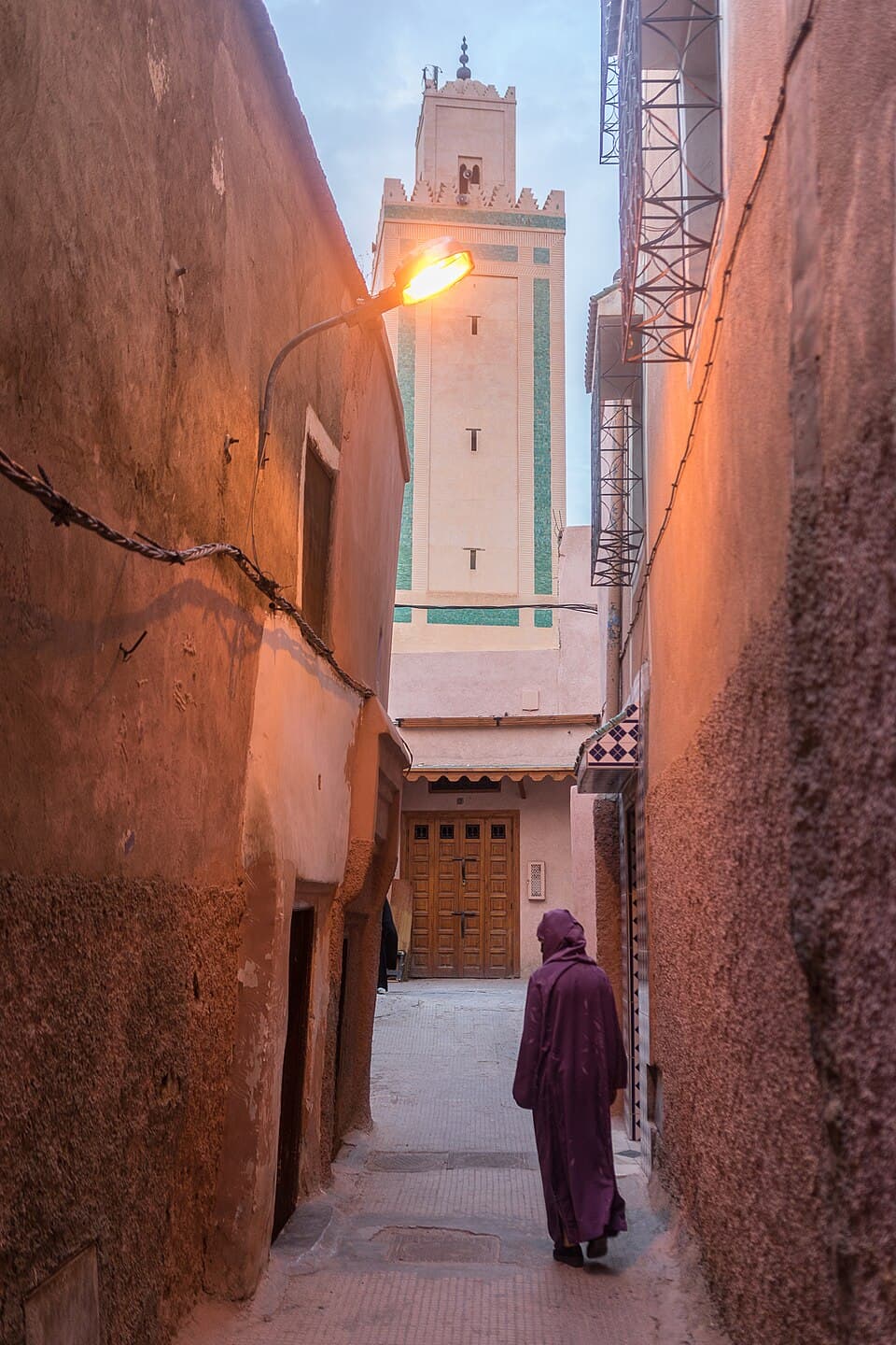 A narrow Marrakech medina alley at first light, a lone figure walking toward a minaret